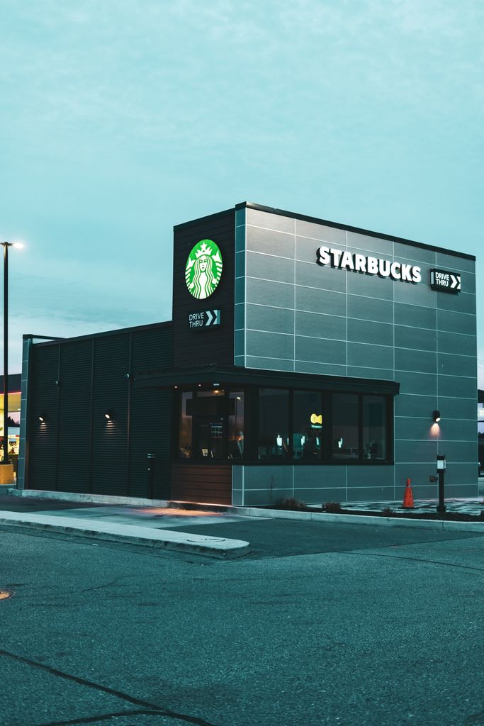 A sleek, modern Starbucks building with a drive-thru, captured in an urban setting at dusk.