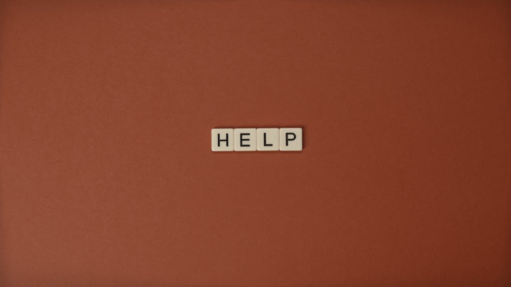 The word 'HELP' spelled with Scrabble tiles on a brown surface, offering conceptual and copyspace.
